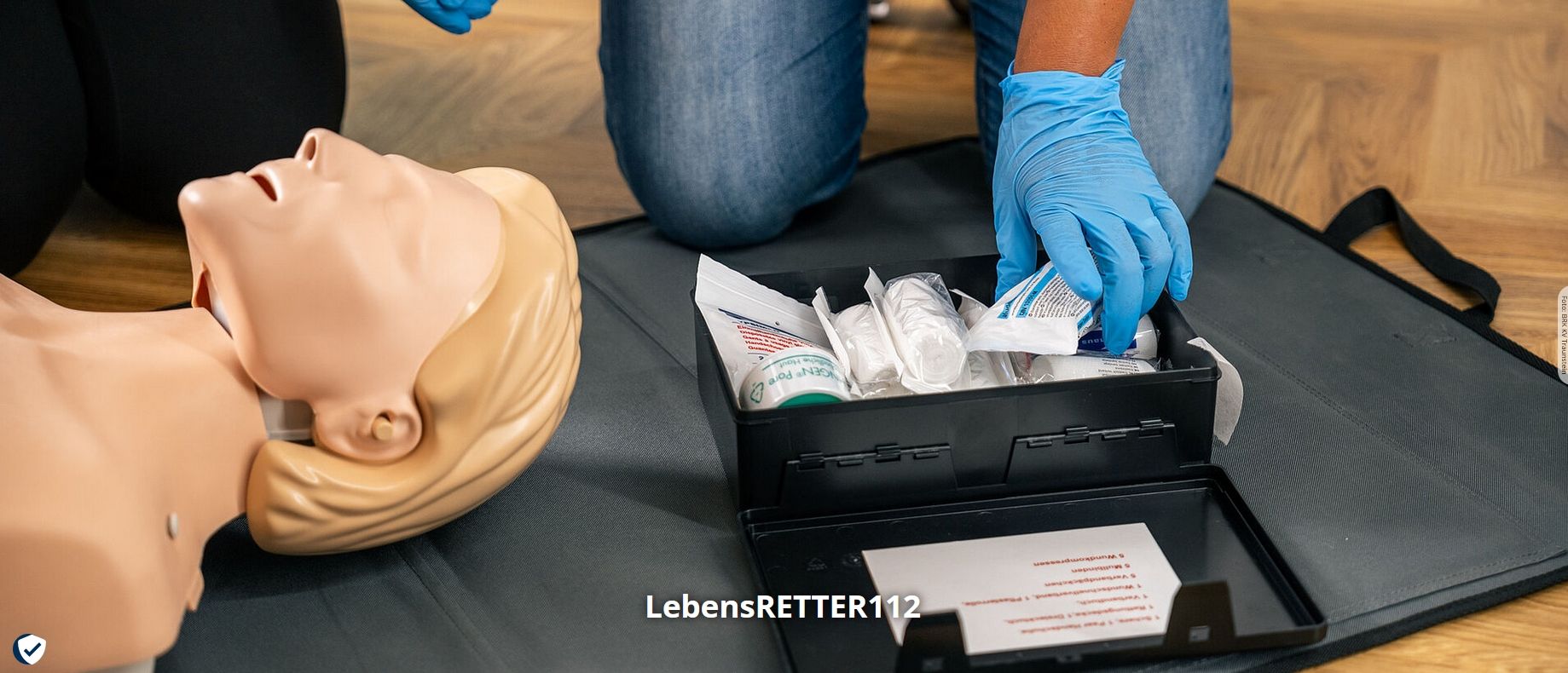 Erste-Hilfe Puppe liegt am Boden mit Utensilien des BRK
